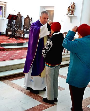 părintele paroh Cristian Dumea presărând cenușa sfințită pe capul unui credincios